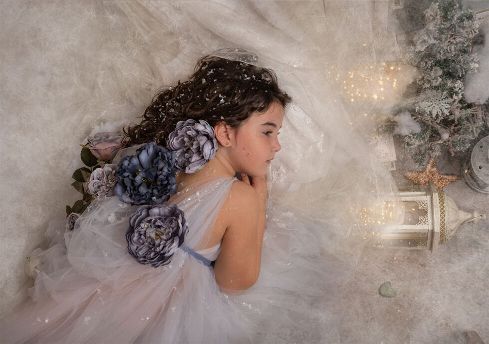 Fotografía niña acostada con vestido blanco entre rosas azules