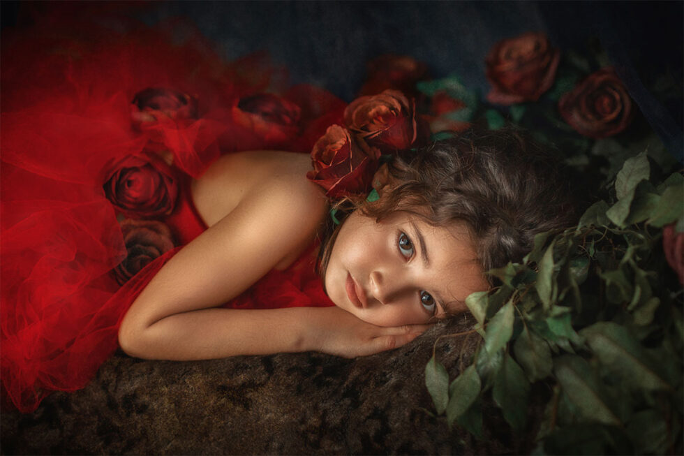 Fotografía chica jóven vestido con rosas rojas acostada en el suelo tierra