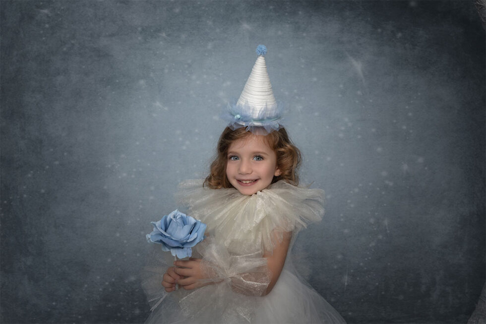 Fotografía chica joven con vestido blanco y rosa azul y gorro en fondo azul