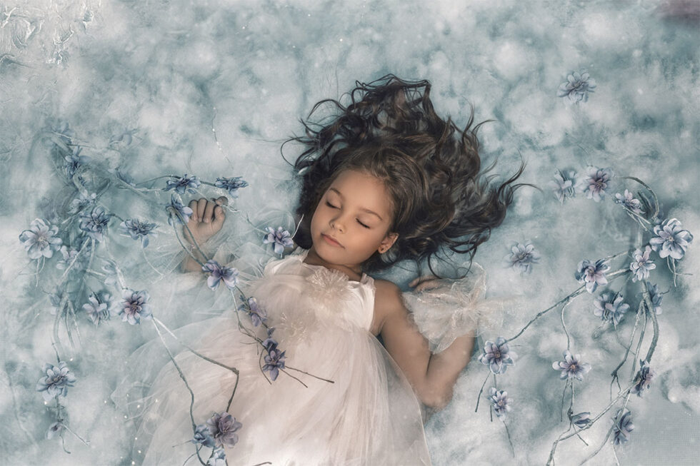 Fotografía niña vestido blanco dormida entre flores fondo con nubes azules