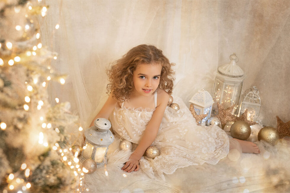 Fotografía niña vestido blanca apoyada en el suelo con luces fondo crema luces