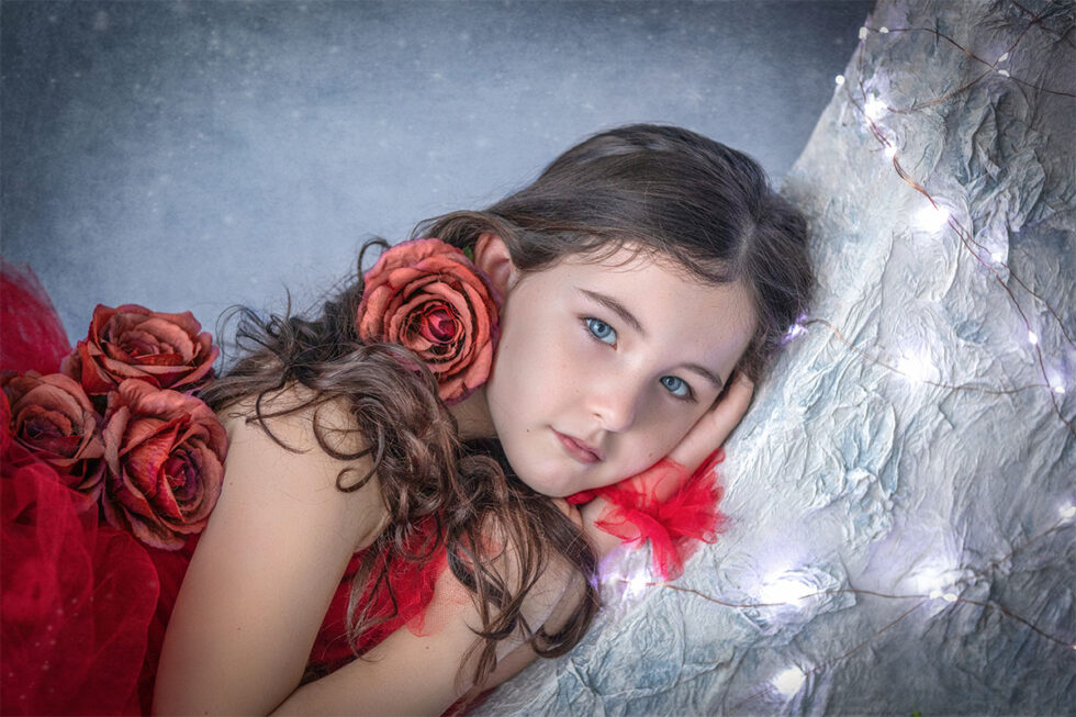 Fotografía niña joven vestido rojo con rosas acostada fondo azul