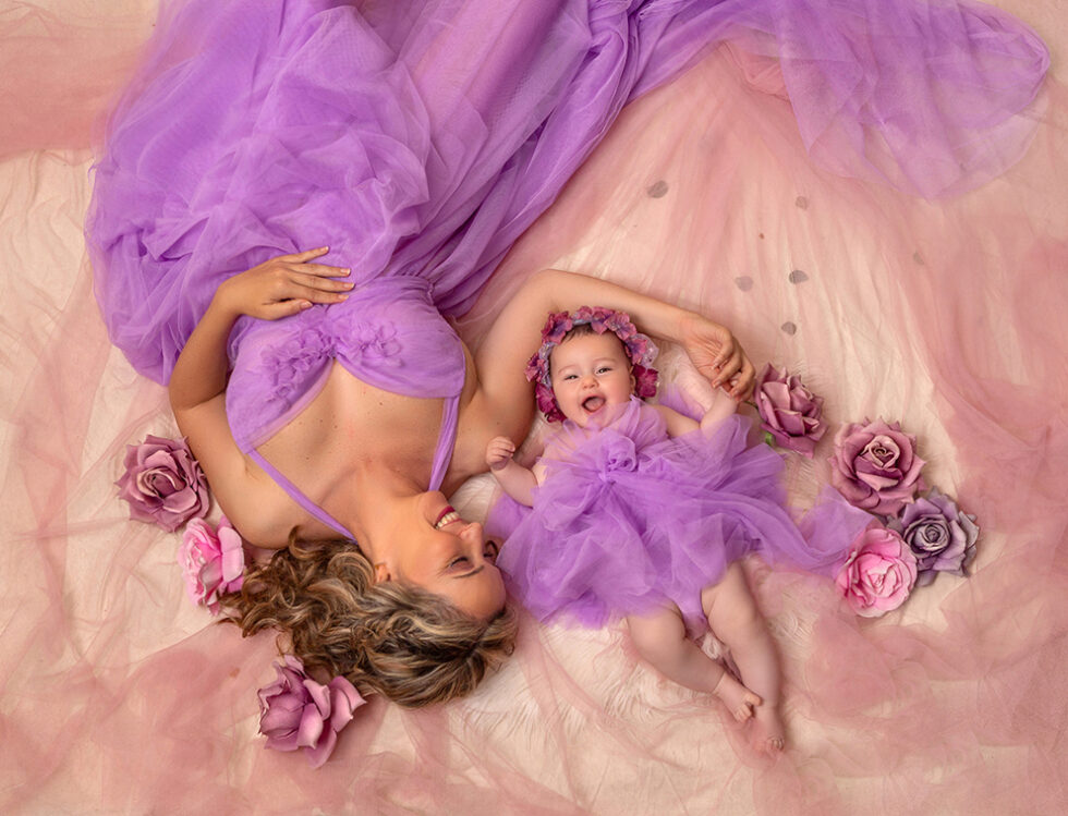 Fotografía madre e hija vestidos morados acostadas entre flores tejido rosa