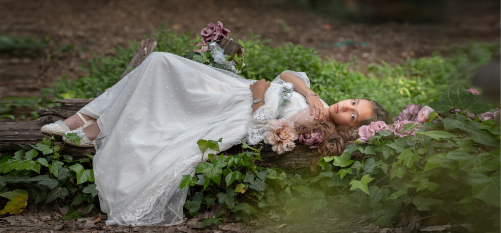 Fotografía de una chica con vestido blanco acostada sobre un tronco